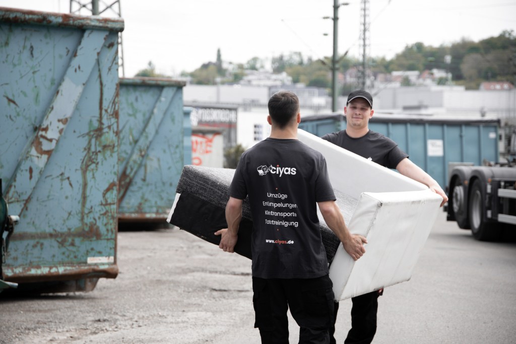 Zwei Mitarbeiter der Ciyas GmbH tragen ein Sofa in Herrenberg zu einem Entsorgungscontainer, da das Sofa entrümpelt wurde.